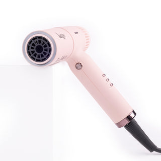 Slim blush t-shape hair dryer with black air vents leaning on white block