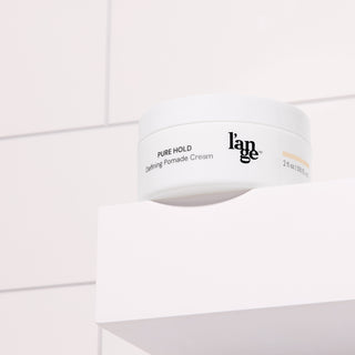 Defining Pomade Cream in a white round jar, placed on a white bathroom shelf with tile background