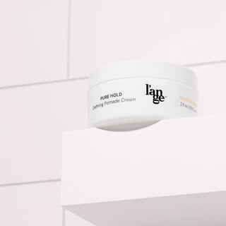 Defining Pomade Cream in a white round jar, placed on a white bathroom shelf with tile background