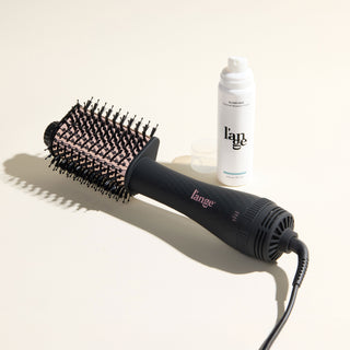 The Effortless Blowout Duo Value Set, featuring a Black Le Volume Eleve brush and Glass Hair spray, displayed against a beige background