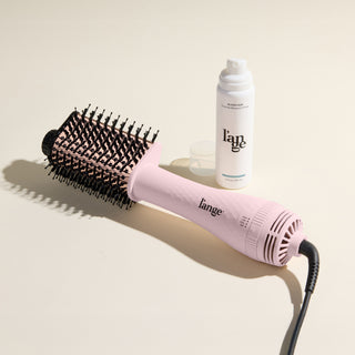 The Effortless Blowout Duo Value Set, featuring a Blush Le Volume Eleve brush and Glass Hair spray, displayed against a beige background