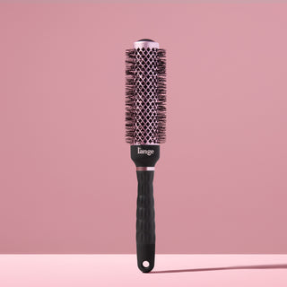 Black round brush for styling hair with a blow dryer against a blush background. 