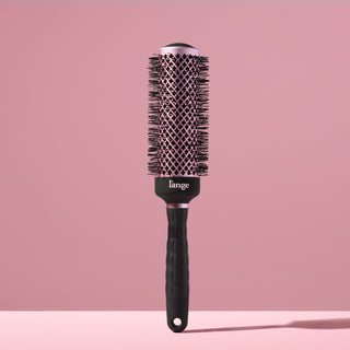 Black round brush for styling hair with a blow dryer against a blush background. 