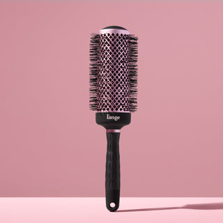 Black round brush for styling hair with a blow dryer against a blush background. 
