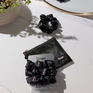 black L’ange satin scrunchies on a vanity beside a small black zip pouch
