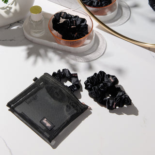 black L’ange satin scrunchies on a vanity beside a small black zip pouch