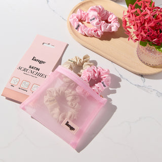 blush and champagne L’ange satin scrunchies on a vanity beside a small pink zip pouch