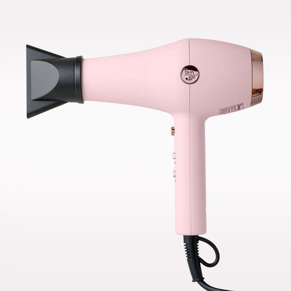 A pink hair dryer with a black attachment, featuring a circular control button and a black power cord, shown against a plain white background.
