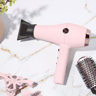 Blush L’ange hair dryer on a marble surface with hair clips and a round brush nearby.