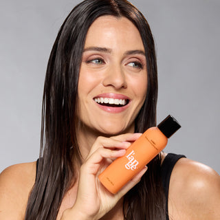 Smiling woman holding an orange bottle of L’ange hair product.