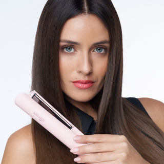 Woman with straight, glossy hair holding a blush L’ange flat iron.