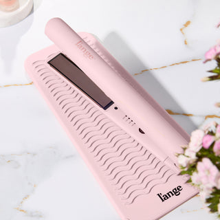 Pink hair straightener resting on a matching textured heat-resistant mat, featuring a sleek design with brand logo.