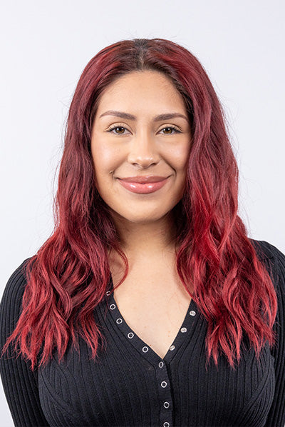 Person with long, wavy red hair and a black buttoned top, smiling against a plain white background.