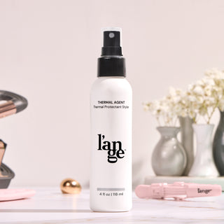 L’ange Thermal Protectant Styler spray, 4 fl oz (118 ml), with a sleek black and white design, positioned on a countertop with blurred styling tools and decorative vases in the background.