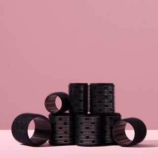 A collection of black thermal hair rollers, arranged on a pink background