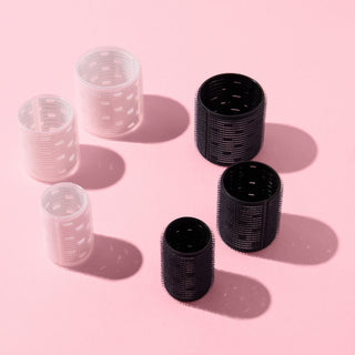 A collection of pink and black thermal hair rollers, arranged on a pink background