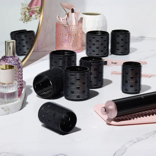 A collection of black thermal hair rollers, arranged on a white marble vanity