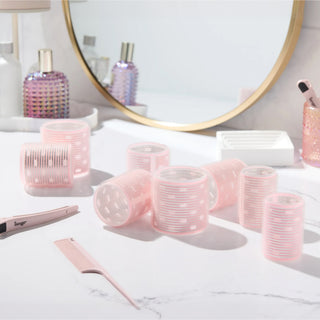 A collection of pink thermal hair rollers, arranged on a white marble vanity