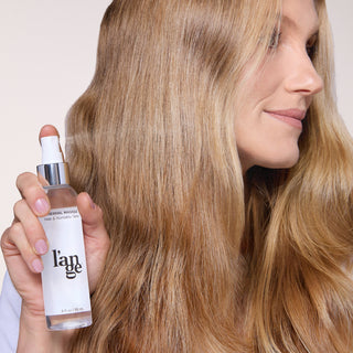 model with soft hair posing with a bottle of Thermal Magique Heat and Humidity Protectant