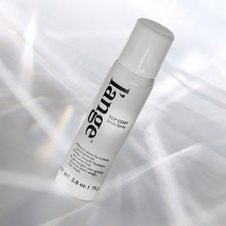 L'ange Top Coat Shine Spray bottle angled on a reflective surface with light prism effects.