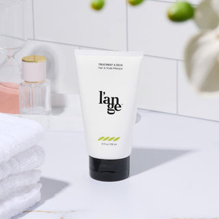 L’ange Treatment à Deux Hair & Scalp Masque displayed on a bathroom counter with towels and decor.