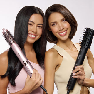 Two women smiling and holding L’ange styling tools, one with a volumizing brush attachment and one with a smoothing brush attachment