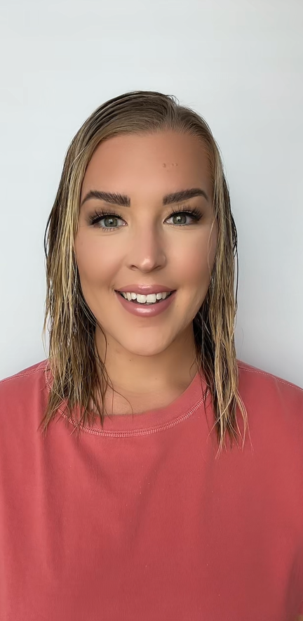 Smiling person with wet hair wearing a coral-colored shirt against a plain background.