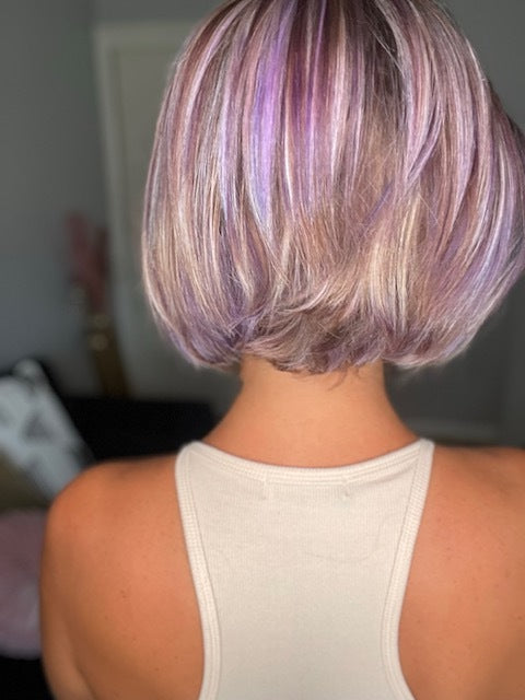 A person with a short, stylish bob haircut featuring shades of lavender and platinum, wearing a beige tank top.