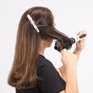 An example of a woman using an alligator clip to section her hair while she uses a brush dryer.