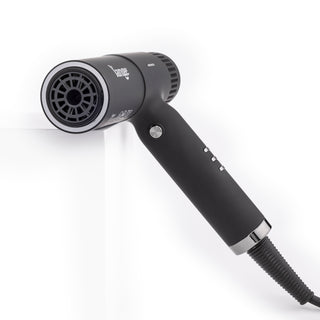 Slim black t-shape hair dryer with black air vents leaning on white block